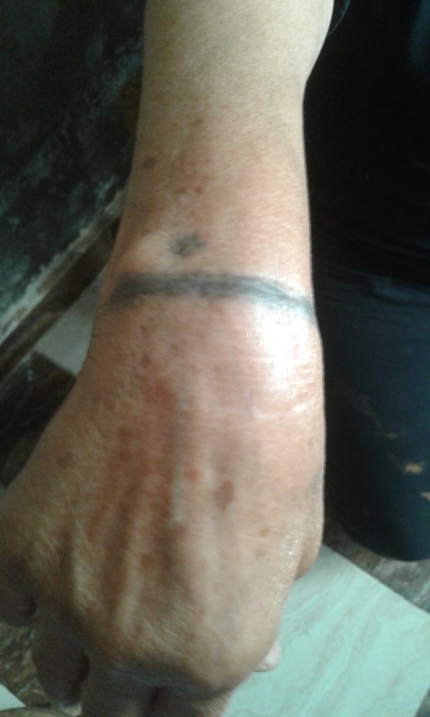 A photo of an Egyptian Coptic's wrist. They have a tattoo on their wrist. It is a black line and a black dot. 