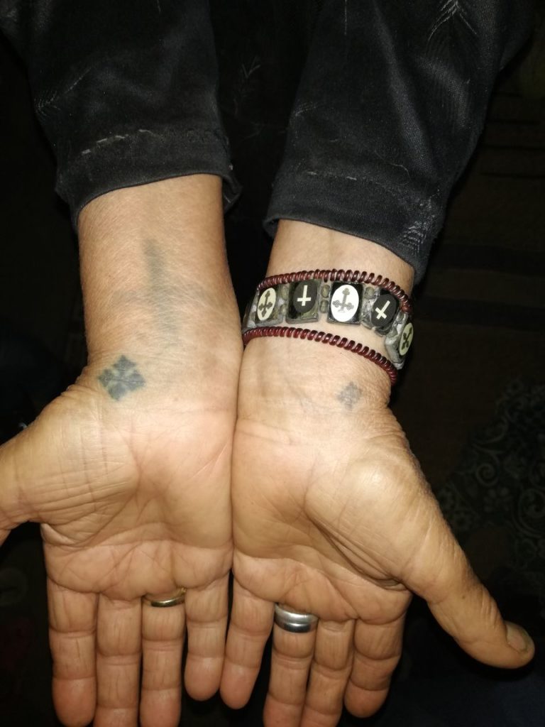 A photo of Zahia's wrsits, showing their tattoos. There are three, all of crosses. There is also a bracelet being worn with crosses on it. Credit: Abanob Alfy